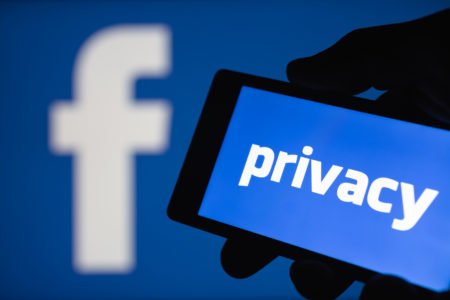 A smartphone in hand displaying the privacy text. Logo of the Facebook blurred on background. The concept of privacy on popular social network.